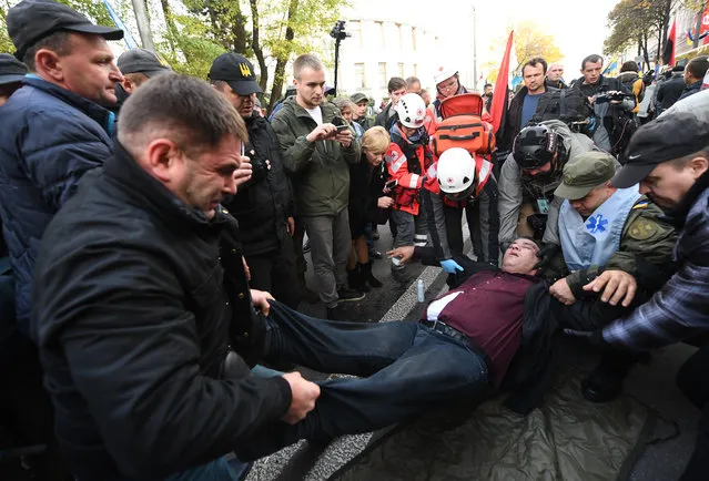 Protesters carry an injured man following clashes with police during a rally of Ukrainian opposition in front of the parliament in Kiev on October 17, 2017. Mikheil Saakashvili, the former leader of Georgia, told a rally in Kiev on October 17, 2017 that President Petro Poroshenko needed to make anti-corruption reforms or leave power if Ukrainians were to see change in their country. The rally outside the Ukrainian parliament in Kiev was called by several political parties including Saakashvili's, who used the opportunity to rally supporters after dramatically returning to Ukraine in September. (Photo by Sergei Supinsky/AFP Photo)