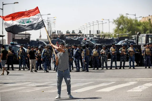A protester, one of supporters of Shiite Muslim cleric Moqtada Sadr, waves an Iraqi national flag before Iraqi security forces deploying along the Jumhuriya (Republic) bridge leading to the capital Baghdad's high-security Green Zone on September 28, 2022, during a protest in Tahrir Square ahead of a parliament session. (Photo by Ahmad Al-rubaye/AFP Photo)