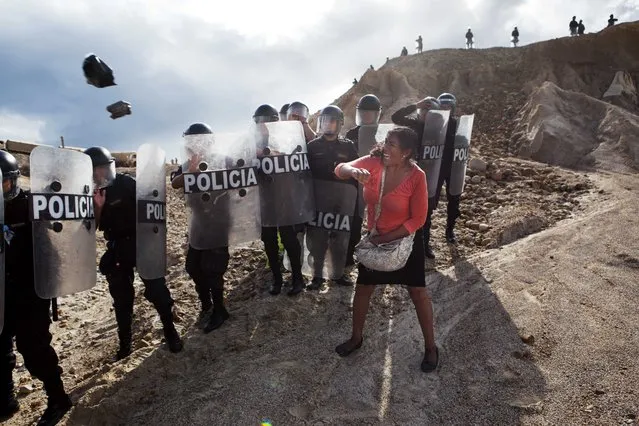 In this April 28, 2014 file photo, a woman throws a rock and a bag at riot policemen who block her way home in Huepetuhe district in Peru's Madre de Dios region in Peru. Soldiers, police and marines have begun destroying illegal gold mining machinery in Peru's southeastern jungle region of Madre de Dios. Authorities began enforcing a ban on illegal mining Monday in the Huepetuhe district. Before the deadline, miners clashed with police while intermittently blocking traffic on the Interoceanic Highway that links the Pacific with Brazil. (Photo by Rodrigo Abd/AP Photo)