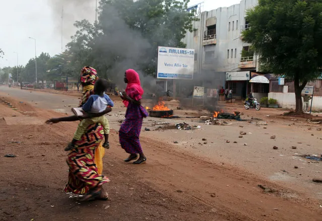 Women and a child past by a burning tyre on a road, after a protest, in Bamako, Mali, Wednesday, August 17, 2016. Protests in Mali's capital against the arrest of a popular activist radio host have turned violent, leaving at least three people dead and several injured. ﻿(Photo by Baba Ahmed/AP Photo)