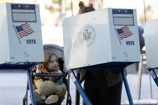 A girl watches her mother casting her ballot during early voting at the Brooklyn Museum in Brooklyn, New York City, U.S., October 29, 2022. (Photo by Jeenah Moon/Reuters)