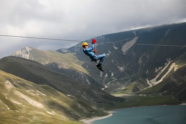 A man rides a zip line on Lake Kezenoyam in the Caucasus Mountains, Chechen Republic, Russia on August 16, 2020. A zip line allows to ride down a steel cable using a pulley at a speed up to 60 km/h. (Photo by Yelena Afonina/TASS)