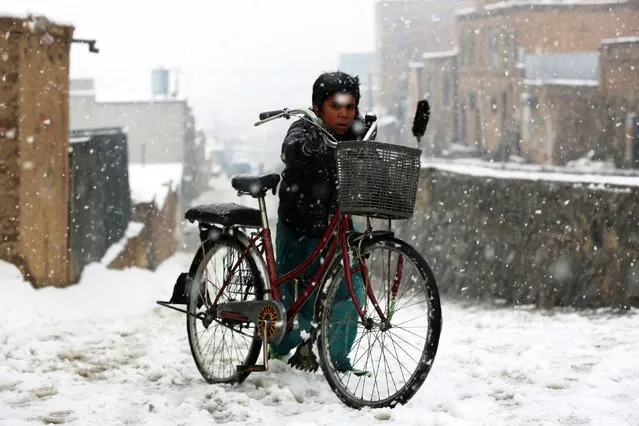 A boy pushes his bicycle along a street during snowfall in Kabul on December 29, 2022. (Photo by AFP Photo/Stringer)