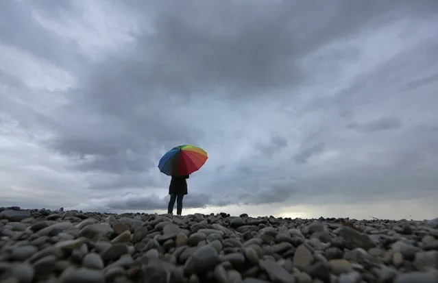 A woman protects herself under an umbrella on the beach in Nice while heavy rain and storm hit southeastern France November 15, 2014. (Photo by Eric Gaillard/Reuters)