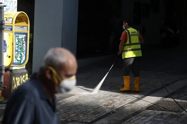 A municipal worker sprays disinfectant on a pavement as a man wearing face mask to prevent the spread of the new coronavirus walks at Ermou Street, Athens' main shopping area, Monday, September 21, 2020. Greece is tightening restrictions in the greater Athens region, stepping up testing and creating quarantine hotels due to an increase in COVID-19 infections after Athenians returned from their summer holidays. (Photo by Thanassis Stavrakis/AP Photo)