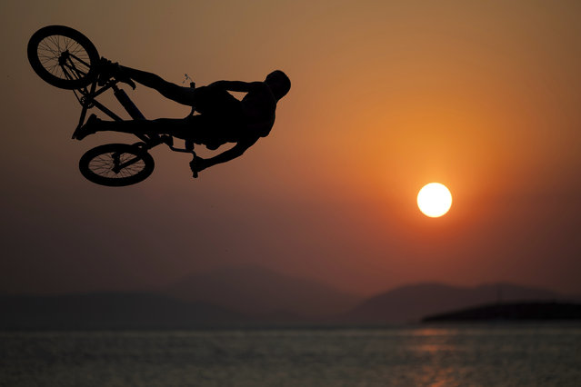 A youth rides his BMX bike to perform a jump into the sea during a hot day at Kavouri beach, south of Athens, Greece, Saturday, July 19, 2025. (Photo by Yorgos Karahalis/AP Photo)