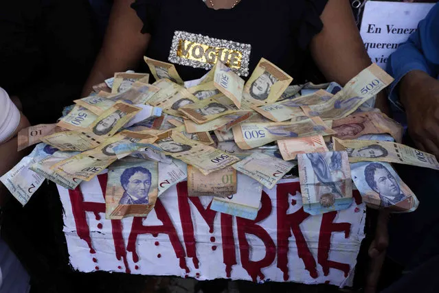 A protester carries a box of Bolivar bills that reads in Spanish read “hunger” during a demonstration for higher salaries and benefits in Caracas, Venezuela, Wednesday, January 11, 2023. (Photo by Ariana Cubillos/AP Photo)