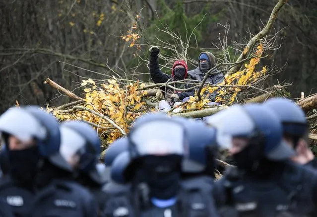 Two activists sit on a pile of cleared trees in front of a chained policeman in Dannenrod, Hessen on November 22, 2020. For more than a year, activists have been using a forest occupation to defend themselves against the ongoing clearing of the forest for the controversial continued construction of the Autobahn 49. In the morning, activists from the “End of Terrain” movement had joined the forest occupants. (Photo by Andreas Arnold/dpa)
