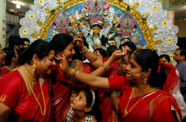 A girl watches as Hindu women apply "sindhur", or vermillion powder, on each others face after worshipping the idol of the Hindu goddess Durga on the last day of the Durga Puja festival in Kolkata, India October 11, 2016. (Photo by Rupak De Chowdhuri/Reuters)