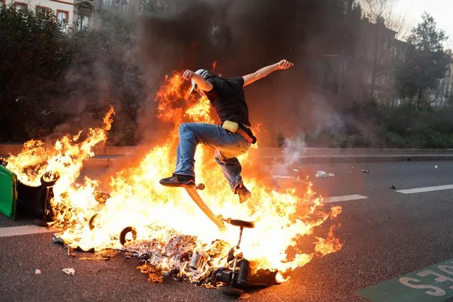 A protestor rides with a skateboard, over burning garbage bins during a demonstration after the government pushed a pensions reform through parliament without a vote, using the article 49.3 of the constitution, in Toulouse, southern France, on March 28, 2023. France faces another day of strikes and protests nearly two weeks after the president bypassed parliament to pass a pensions overhaul that is sparking turmoil in the country, with unions vowing no let-up in mass protests to get the government to back down. The day of action is the tenth such mobilisation since protests started in mid-January against the law, which includes raising the retirement age from 62 to 64. (Photo by Charly Triballeau/AFP Photo)