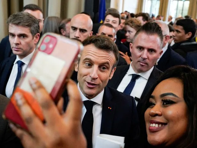 French President Emmanuel Macron, candidate for his re-election in the 2022 French presidential election, reacts while taking a selfie with a woman during a campaign meeting with local residents in Pau, France, March 18, 2022. (Photo by Vincent West/Reuters)
