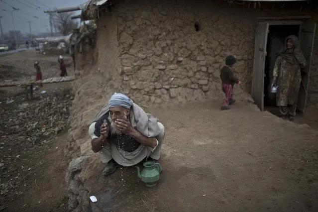 An elderly Afghan refugee man performs his wado, or cleaning himself before praying, outside his mud house in a slum on the outskirts of Islamabad, Pakistan, Wednesday, January 21, 2015. (Photo by Muhammed Muheisen/AP Photo)