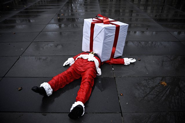 This photograph shows French street artist James Colomina's Santa Claus work, depicting a Santa Claus lying on the ground, his head and torso crushed by a huge white gift box adorned with a red ribbon on the Place de la Republique in Paris, on December 19, 2024. (Photo by Julien de Rosa/AFP Photo)