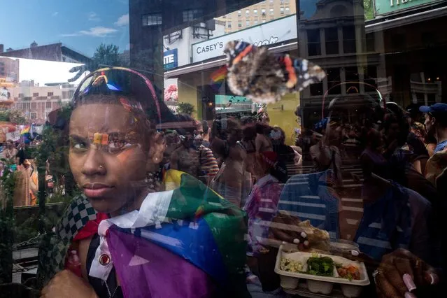 A person looks out a window at people participating in the 2023 NYC Pride Parade in Manhattan in New York City, U.S., June 25, 2023. (Photo by David Dee Delgado/Reuters)