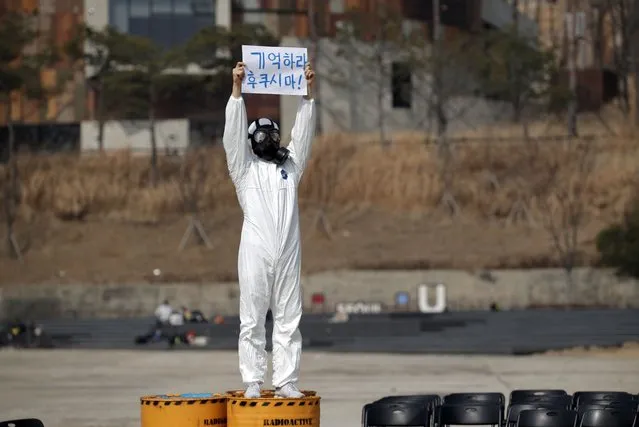 An environmental activist wearing gas mask holds a sign as he performs after a news conference marking the 10th anniversary of Fukushima nuclear disaster caused by the March 11 earthquake and tsunami in Japan, at a park in Seoul, South Korea, Thursday, March 11, 2021. Japan on Thursday marked the 10th anniversary of a massive earthquake, tsunami and nuclear disaster that struck Japan's northeastern coast. The letters read “Remember Fukushima”. (Photo by Lee Jin-man/AP Photo)