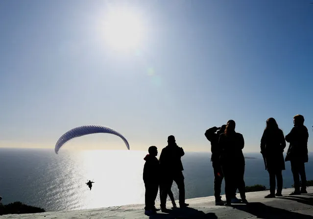 People watch as a paraglider flies near Signal Hill, in Cape Town, South Africa on July 10, 2023. (Photo by Esa Alexander/Reuters)