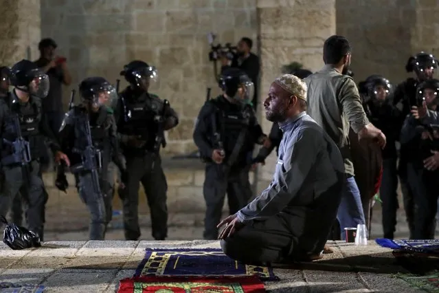 A Palestinian man prays as Israeli police gather during clashes at the compound that houses Al-Aqsa Mosque, known to Muslims as Noble Sanctuary and to Jews as Temple Mount, amid tension over the possible eviction of several Palestinian families from homes on land claimed by Jewish settlers in the Sheikh Jarrah neighborhood, in Jerusalem's Old City, May 7, 2021. (Photo by Ammar Awad/Reuters)