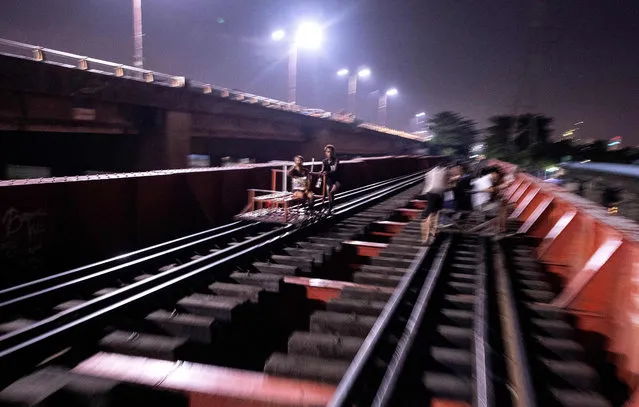 This picture taken on October 18, 2018 shows a “trolley boy” (C) pushing a home- made cart along a train track in Manila. Scores of commuters in the city of about 12 million are propelled to their destinations daily by so-called “trolley boys” pushing metal carts that ply a few segments of the sprawling capital's railroads. (Photo by Noel Celis/AFP Photo)