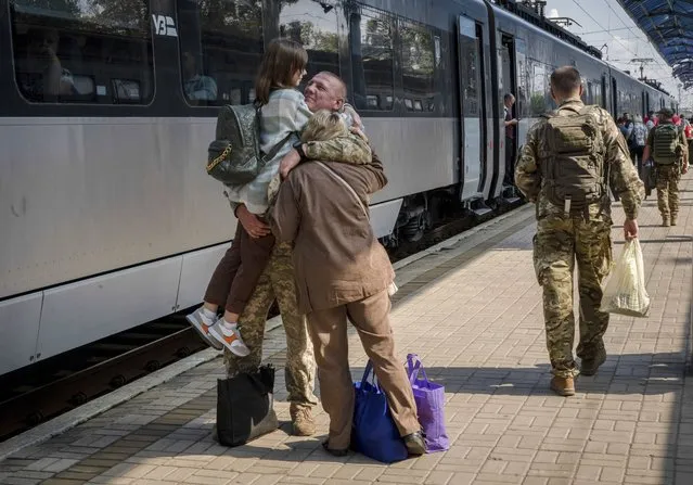 A Ukrainian serviceman hugs his wife and the daughter at the railway station in Sloviansk, Donetsk region, Ukraine on Tuesday, September 12, 2023. The train that runs from Ukraine's capital, Kyiv, to the city of Kramatorsk in the east stands apart from others in Ukraine. It is shrouded in solemn silence as passengers anticipate their final destination – in front-line areas where battles rage between Ukrainian and Russian forces. (Photo by Hanna Arhirova/AP Photo)