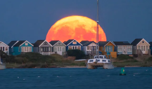 The Buck full moon rises above Mudeford beach huts in Dorset, southwest England on July 13, 2022. The Buck Moon is named by Algonquin tribes of North America, referring to a male deer whose antlers will grow to full size by July, ready to compete with other males during autumn's breeding season. This full Moon is also known as the Raspberry Moon or the Thunder Moon. (Photo by Steve Hogan/The Times)