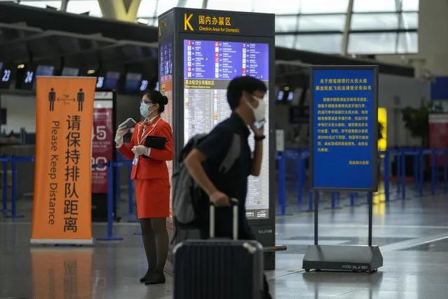 A passenger wearing a face mask to help curb the spread of the coronavirus pushes his luggage past a masked airliner staff stand near quiet check-in counters at Pudong International Airport in Shanghai, China, Sunday, July 25, 2021. Airline flights were canceled in eastern China and cargo ships were ordered out of the area Saturday as Typhoon In-fa churned toward the mainland after dumping rain on Taiwan. (Photo by Andy Wong/AP Photo)