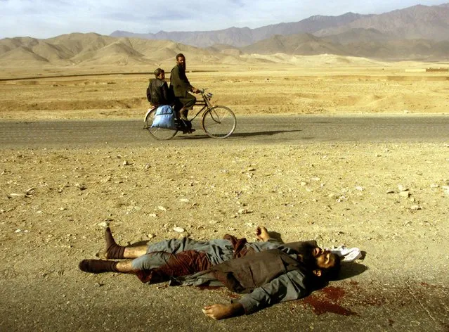 An Afghan man and his son ride a bicycle past the body of a Taliban fighter killed near Kabul as Northern Alliance fighters approached the Afghan capital in November 2001. Forces of the anti-Taliban Northern Alliance entered Kabul after defeating Taliban forces north of the capital, civilians greeted opposition fighters and celebrated in the streets. (Photo by Yannis Behrakis/Reuters)