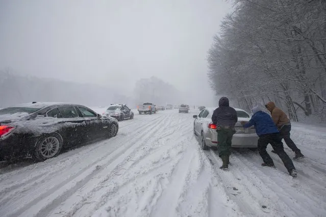Three people try to help move a car out of the snow on I-95 Southbound in Warwick, Rhode Island, USA, 09 February 2017 as a major snowstorm hits the region. (Photo by Lisa Hornak/EPA)
