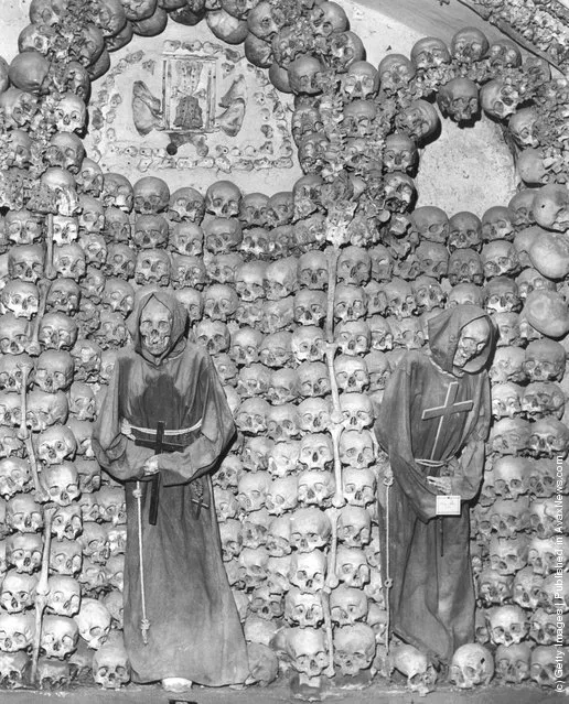 A collection of human skulls and bones surround the hooded, cloaked skeletons of two monks at a Capuchin monastery