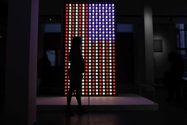A British Museum representative poses for photographs next to an illuminated American flag at the entrance of “The American Dream: pop to the present” exhibition during a media photocall at the British Museum in London, Monday, March 6, 2017. (Photo by Matt Dunham/AP Photo)