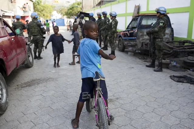 In this February 22, 2017 photo, children play in the street while U.N. peacekeepers from Brazil patrol in the Cite Soleil slum, in Port-au-Prince, Haiti. It took U.N. troops three years to gain control over the sprawling district of Cite Solel, but it's now placid even though its residents still live in desperate poverty. (Photo by Dieu Nalio Chery/AP Photo)