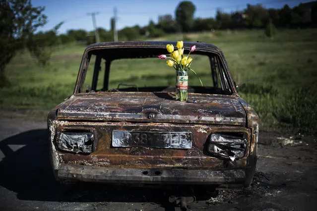 A bouquet of flowers is placed atop the burnt out shell of a car at a location where clashes between pro Russia gunmen and the Ukrainian army took place, four kilometers (2.5 miles) north of Slovyansk, Ukraine, Wednesday, May 7, 2014. (Photo by Manu Brabo/AP Photo)