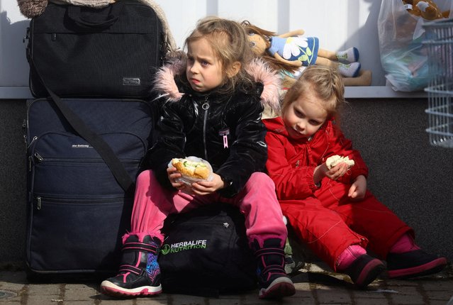 Two girls eat sandwiches provided by volunteers after fleeing from Ukraine because of the Russian invasion as they arrive with a bus at the village of Moszczany near the border checkpoint at Korczowa, Poland, March 1, 2022. (Photo by Kai Pfaffenbach/Reuters)