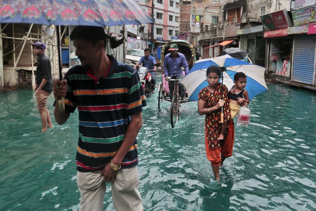Bangladeshi people walk through a waterlogged street after heavy rainfall in Dhaka, Bangladesh, Saturday, May 21, 2016. A cyclone unleashed heavy rain and strong winds on Bangladesh's southern coastal region on Saturday, killing at least 11 people and forcing hundreds of thousands from their homes. Mixing of rain water and toxic waste from industries has turned water into green. (Photo by A.M. Ahad/AP Photo)
