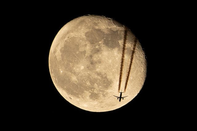 An aircraft flies above Iraq's southern city of Basra past the waning gibbous moon late on April 18, 2022. (Photo by Hussein Faleh/AFP Photo)