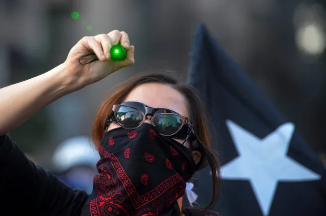 A demonstrator points a green laser light to riot police during a protest against the government of President Piñera on November 27, 2019 in Santiago, Chile. Earlier today, President Piñera urged Congress to approve bills to reduce social unrest by banning hooded protesters, looting and barricades. He insisted on bringing military to the streets to protect public goods without calling state of emergency. Protests continue uninterruptedly since October 18 when a raise in metro fare was announced. Demonstrators demand urgent measures to reduce inequality, a raise in pensions and minimum salary, fair prices in public services and improvements in education and health care.(Photo by Claudio Santana/Getty Images)