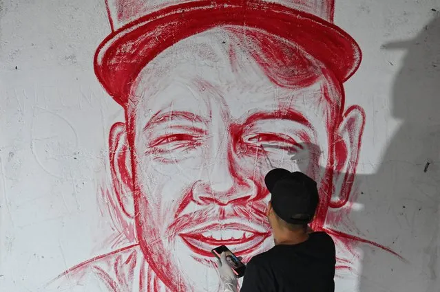 Colombian artist Julian Castillo paints with human blood donated by volunteers a mural depicting Puerto Rican singer Rene Perez, aka Residente, at the Siloe neighborhood in Cali, Colombia, on March 23, 2022, in rejection of violence. (Photo by Luis Robayo/AFP Photo)