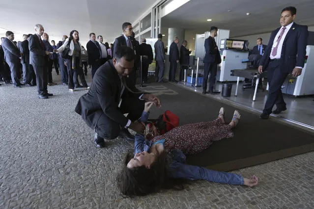 Shouting that she did not want to die before speaking to Brazil's President Michel Temer, Janeth Rosa de Souza throws herself on the floor after being stopped by security agents from entering the Presidential Palace Planalto in Brasilia, Brazil, Wednesday, June 7, 2017. De Souza threw herself on the floor minutes before the start of an official ceremony with President Temer. (Photo by Eraldo Peres/AP Photo)
