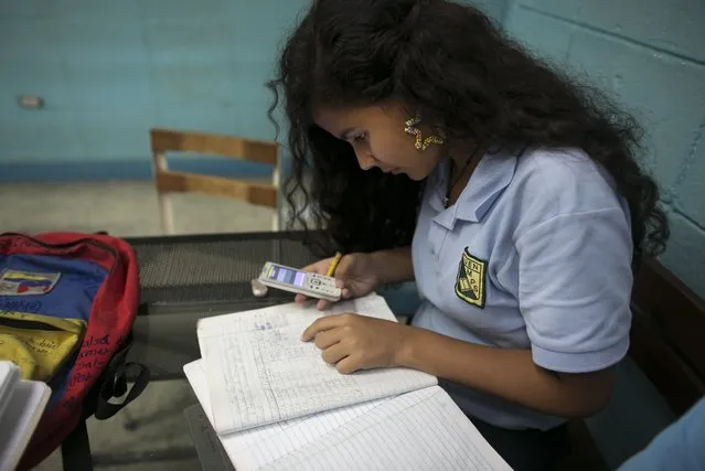 In this May 30, 2016 photo, Maria Arias, 14, quickly uses the calculator on a friend's cell phone to figure out why she has errors on her homework, during her accounting class at a public high school in Caracas, Venezuela. Arias' accounting teacher recently went missing for a week and a half, and when she showed up again, she limited herself to correcting homework. (Photo by Ariana Cubillos/AP Photo)