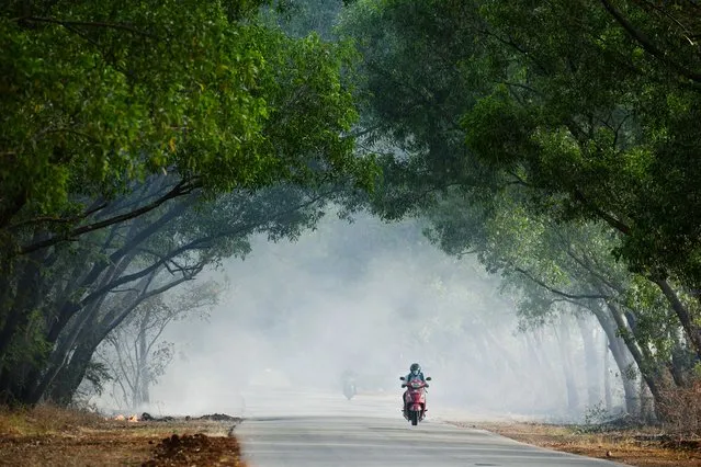 A motorist rides along a road past a thick plume of smoke from burning leaves on the outskirts of Bangalore on March 2, 2022. (Photo by Manjunath Kiran/AFP Photo)