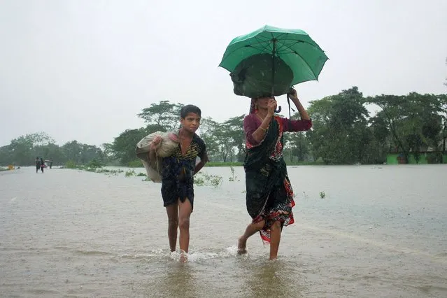 People wade along a road in a flooded area following heavy monsoon rainfalls on the outskirts of Sylhet on June 17, 2022. Bangladesh has deployed troops to help two million people stranded by floods after relentless monsoon rains inundated huge swathes of territory for the second time in weeks, officials said on June 17. (Photo by AFP Photo/Stringer)