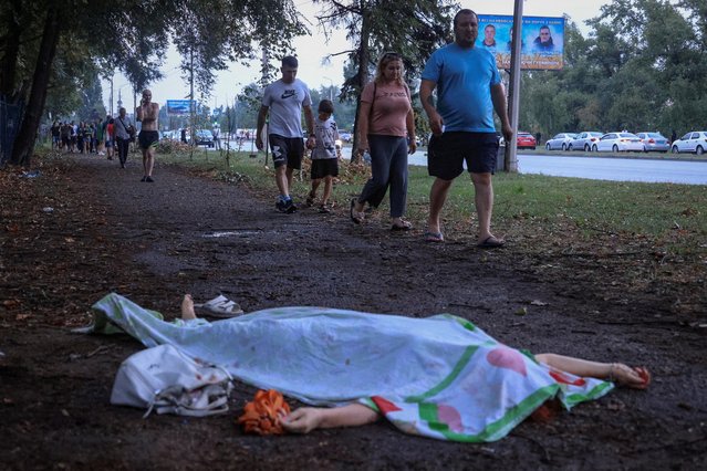 People walk past to the body of Nataliia Tereshchenko, a 66-year-old teacher who was killed during a Russian missile strike in Zaporizhzhia, Ukraine on August 10, 2023. (Photo by Andrii Dubchak/Reuters)