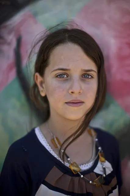 In this Tuesday, July 29, 2014 photo, Amal Qalloosh, 11, poses for a picture at Zaatari refugee camp, near the Syrian border, in Mafraq, Jordan. More than 50,000 refugees under the age of 18 call the wind-swept, massive desert camp home. All have stories about the war, like Amal Qallosh, who fled her home near Daraa, Syria, with her family after a government bombing. “On the way here there was a lot of shelling”, she said. “It was terrifying but we made it all safe to the camp”. (Photo by Muhammed Muheisen/AP Photo)