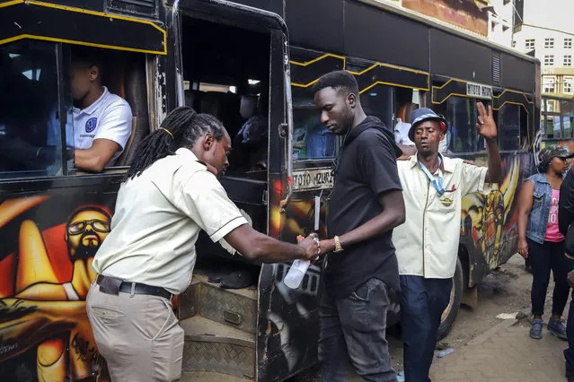 A bus conductor disinfects the hands of a passenger, after the government directed all operators of “matatus”, or public minibuses, to provide hand sanitizer to their clients, on a busy street in downtown Nairobi, Kenya Friday, March 13, 2020. Authorities in Kenya said Friday that a Kenyan woman who recently traveled from the United States via London has tested positive for the new coronavirus, the first case in the East African country. (Photo by Patrick Ngugi/AP Photo)