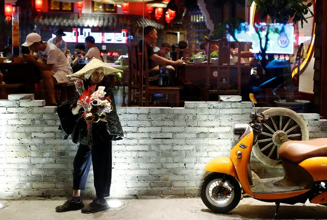 A woman sells flowers outside a restaurant at night in Beijing, China July 14, 2016. (Photo by Thomas Peter/Reuters)