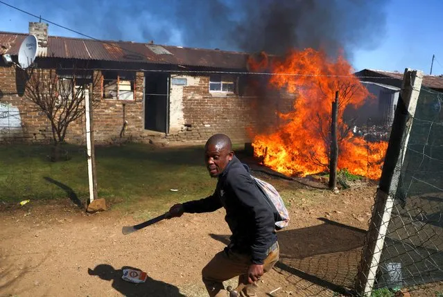 A man holding a machete reacts next to a fire after community members burned shacks and belongings as they searched for alleged illegal miners known as ‘zama-zamas’ as a protest, following alleged rape of eight models on July 28 when a television crew filmed a music video at a mine dump in the nearby township, in the West Rand, South Africa on August 8, 2022. (Photo by Siphiwe Sibeko/Reuters)