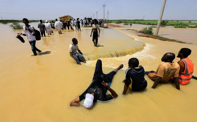 People rest as others cross the water during floods in Al-Managil locality in Jazeera State, Sudan on August 23, 2022. (Photo by Mohamed Nureldin Abdallah/Reuters)