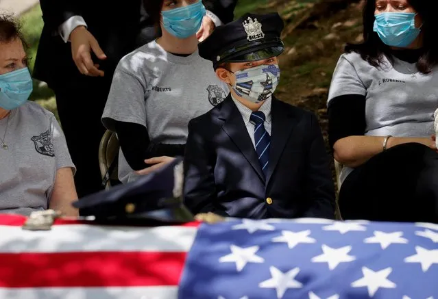 Gavin Roberts wears his father's police hat as he looks at the flag-draped casket of his father, Glen Ridge Police Department officer Charles Roberts, at his funeral service, after the 45-year-old father of three died of the coronavirus in Glen Ridge, New Jersey, May 14, 2020. (Photo by Mike Segar/Reuters)