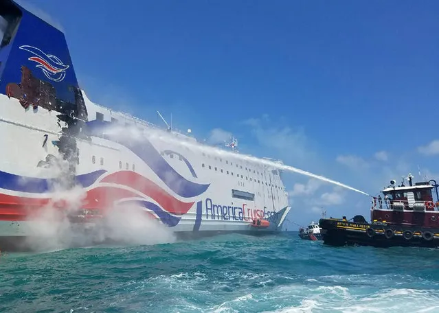 In this photo provided by the U.S. Coast Guard, a local San Juan, Puerto Rico-based tug crew uses a fire hose to cool the hull of the Caribbean Fantasy cruise ship that caught fire, a mile from San Juan Harbor, Puerto Rico, Wednesday, August 17, 2016. More than 500 passengers and crew were evacuated from a burning ship off Puerto Rico's north coast and many required medical care, though there were no reported fatalities or life-threatening injuries. (Photo by Petty Officer 2nd Class Jonathan Lally/US Coast Guard via AP Photo)