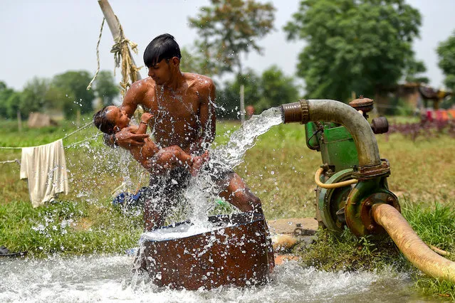 A man gives bath to his son with a water tube well near a field as the temperature rises in New Delhi on June 10, 2020. (Photo by Money Sharma/AFP Photo)
