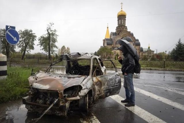 A passerby looks at a car damaged by Russian shelling in central Bakhmut, the site of the heaviest battle against the Russian troops in the Donetsk region, Ukraine, Wednesday, October 26, 2022. (Photo by Efrem Lukatsky/AP Photo)